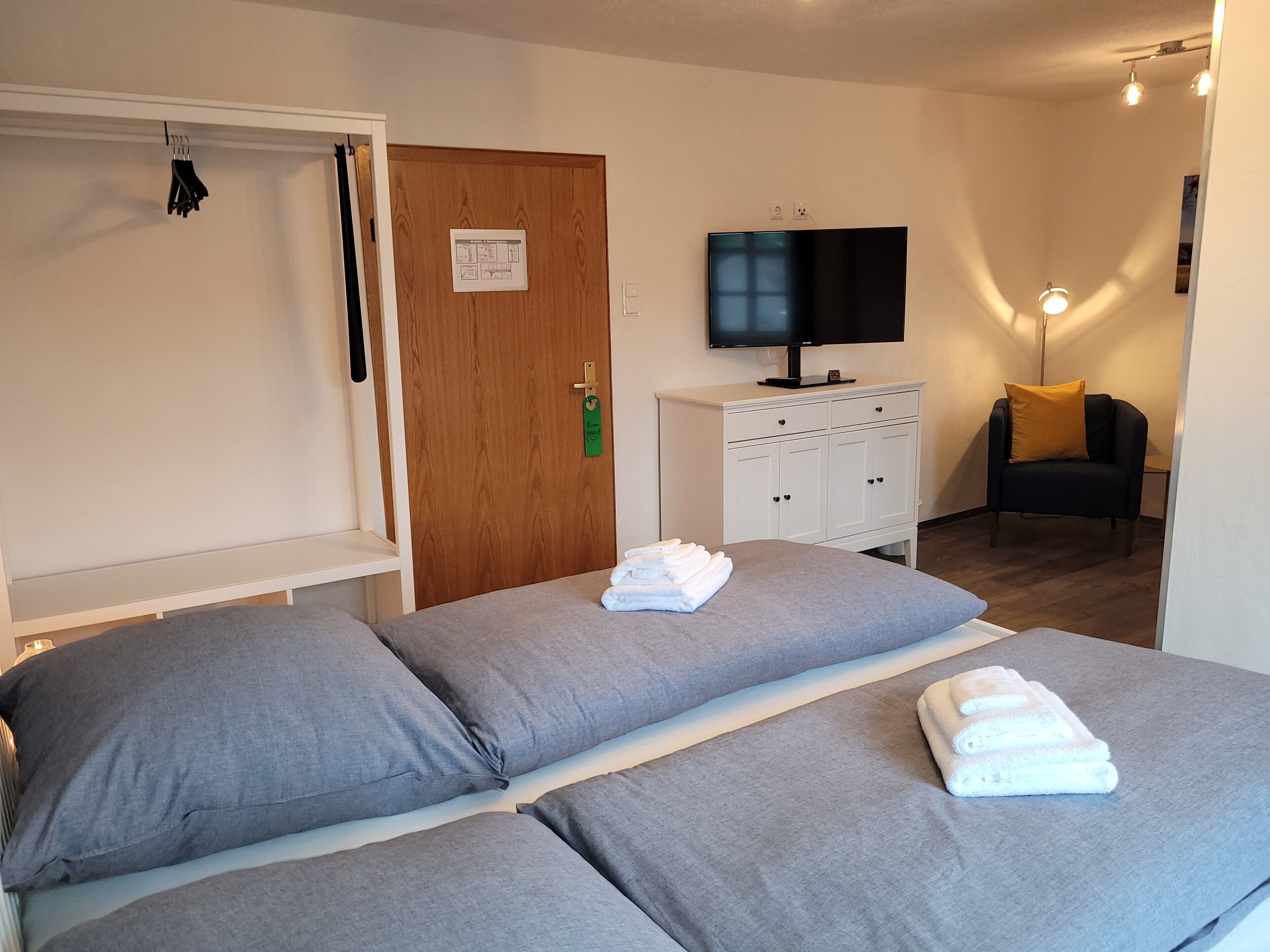 A hotel room with two beds, a TV, a wardrobe, and a chair with a yellow cushion.