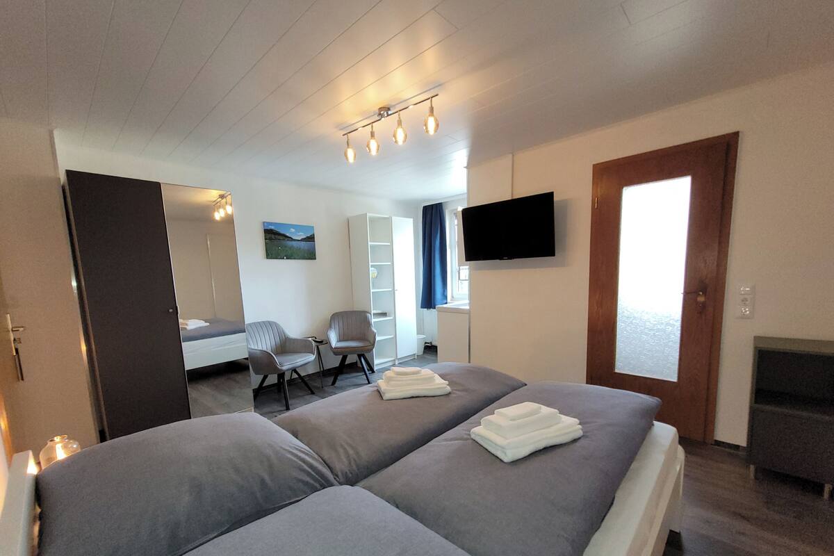 Une chambre d’hôtel avec deux lits, un bureau, une chaise, une télévision et une fenêtre.