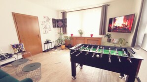 A room with a foosball table, a television displaying a fire, and a window with curtains. - VINEU - Bed n Breakfast (Winterberg)
