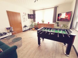 Ein Zimmer mit einem Kicker, einem Fernseher, der ein Feuer zeigt, und einem Fenster mit Vorhängen.
