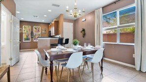 Un comedor con una mesa dispuesta para cuatro personas, una araña y vistas al exterior a través de un ventanal.