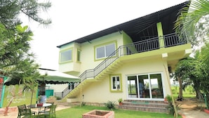 A two-story house with a balcony, a staircase, and a patio area with a table and chairs. - SandPebbles Bhitarkanika Jungle Resorts (Rajnagar)