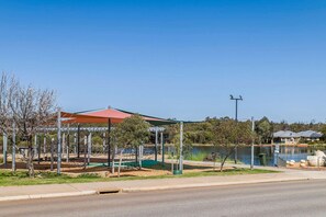 Un parc amb un espai de jocs, una zona coberta i un llac.