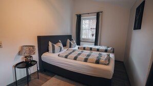 A bedroom with a bed, bedside table, lamp, and a window with curtains.
