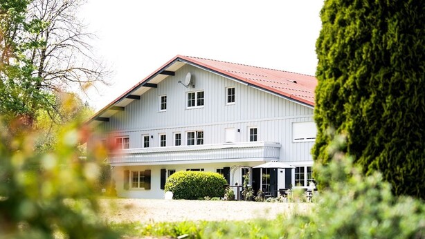 A two-story building with a red roof, multiple windows, and a covered outdoor area with seating.