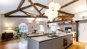 A spacious kitchen with a large island, wooden beams, and a hanging light fixture. - Pepys House: A Modern Touch of History (London)