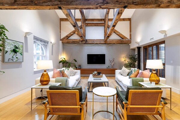 A spacious living room with high ceilings, exposed wooden beams, a large flat-screen TV, and comfortable seating.