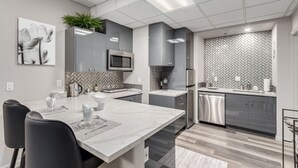 A modern kitchen with grey cabinets, a herringbone backsplash, stainless steel appliances, and a marble island. - Stylish & Prestigious 2 Bed 2 Bath-On The Avenue (Fountain Hills)