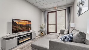 A modern living room with a flat-screen TV, grey sofa, and a fireplace. - Stylish & Prestigious 2 Bed 2 Bath-On The Avenue (Fountain Hills)