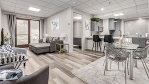 A modern living room with a sofa, a coffee table, and a chessboard. There is a kitchen area with a microwave, a sink, and a dining table with chairs. - Stylish & Prestigious 2 Bed 2 Bath-On The Avenue (Fountain Hills)