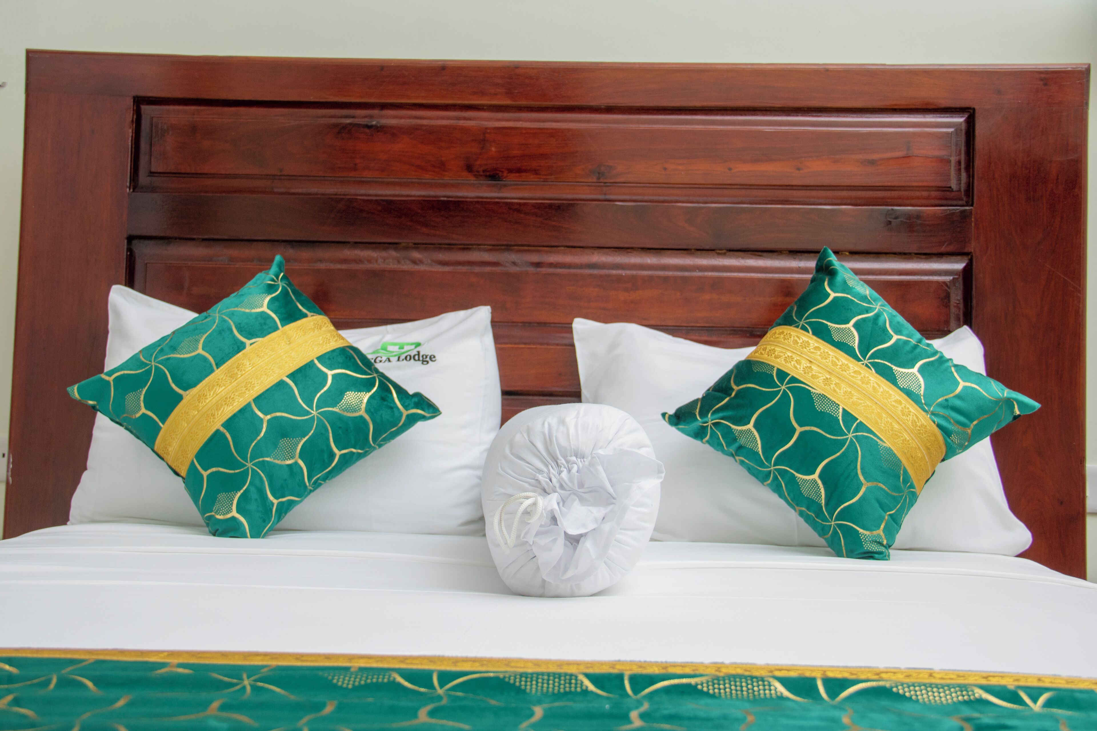 Un lit avec une tête de lit en bois, deux coussins décoratifs à motifs verts et dorés, et un coussin blanc.