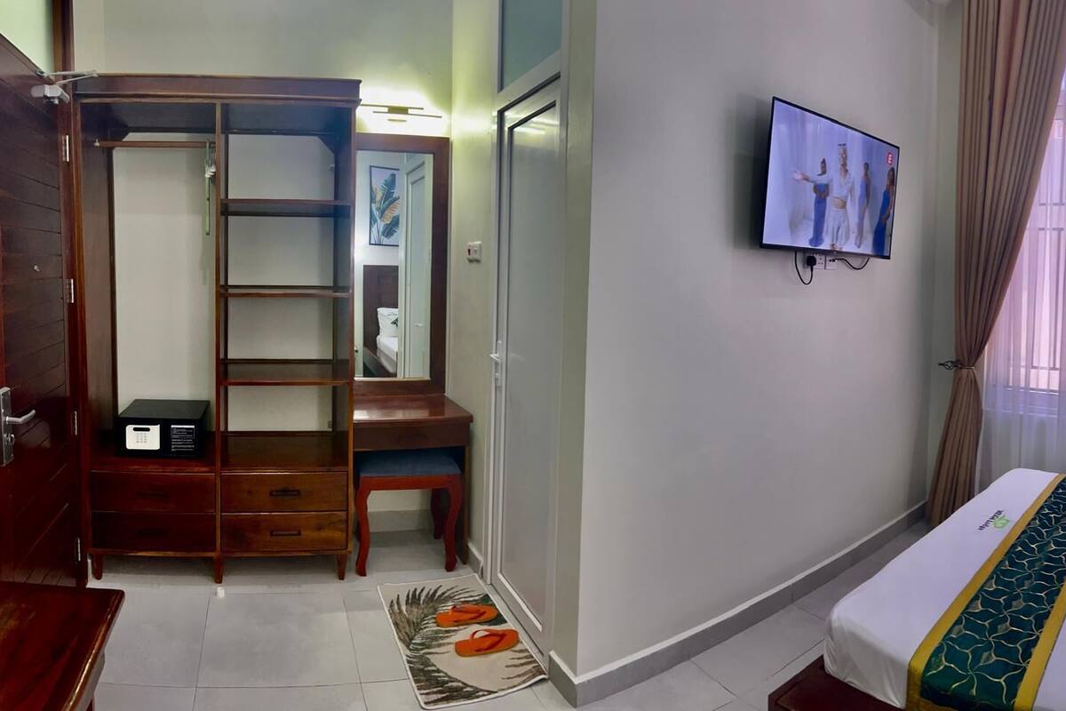 Ein Hotelzimmer mit Bett, Schreibtisch, Kleiderschrank, Fernseher und einem Fenster mit Vorhängen.