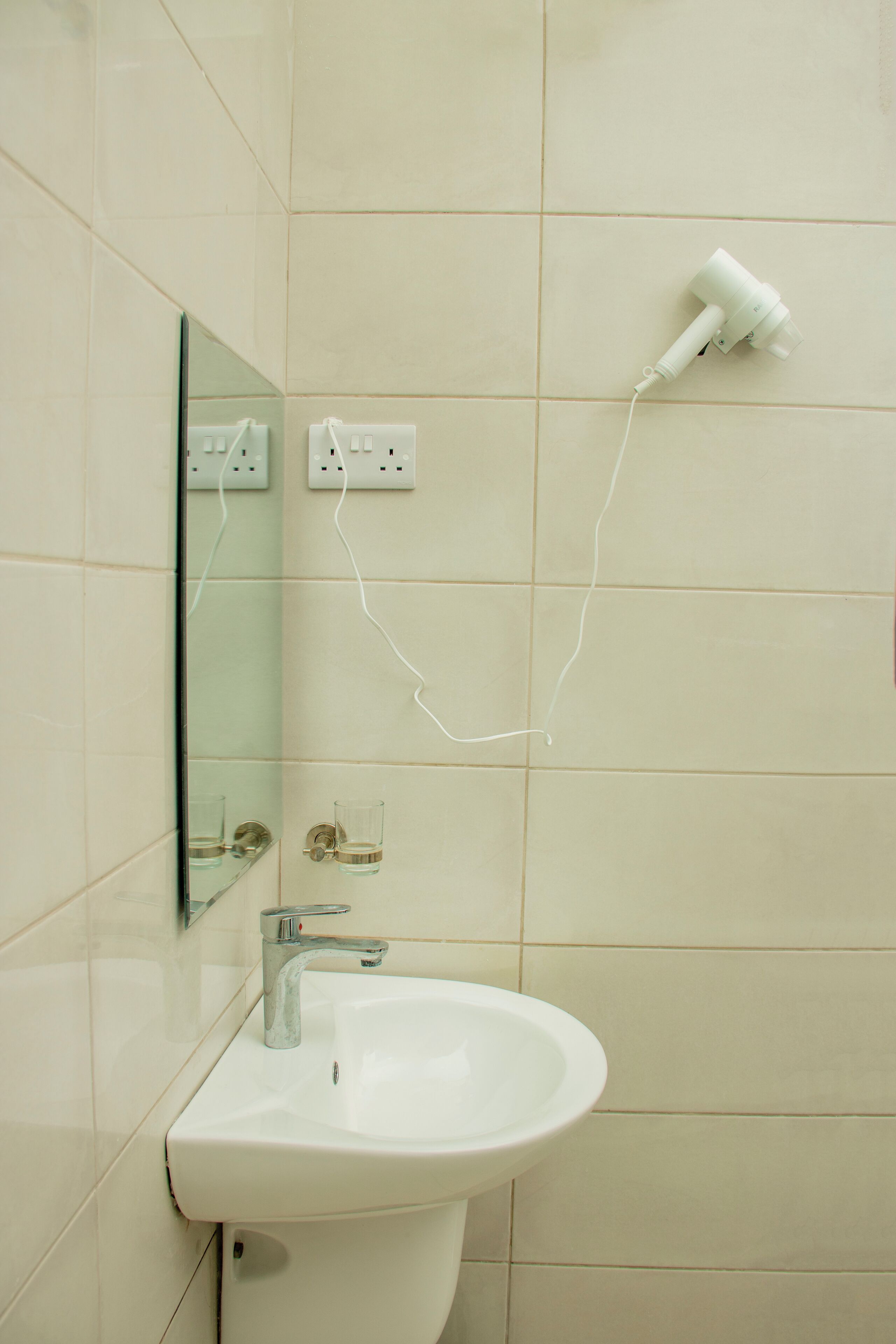 A bathroom with a sink, mirror, and hairdryer plugged into a wall outlet.