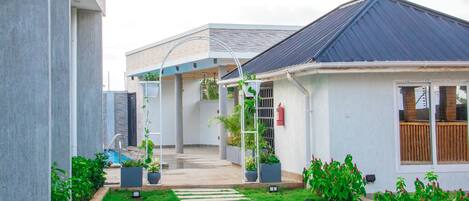 A modern house with a covered patio, a small garden with potted plants, and a pathway leading to the entrance.