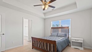 Un dormitorio con cama de madera, mesita de noche, ventilador de techo y ventana con persianas.
