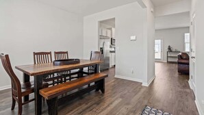 Un comedor con una mesa de madera y bancos, una cocina al fondo, y un sofá de cuero en otra habitación.
