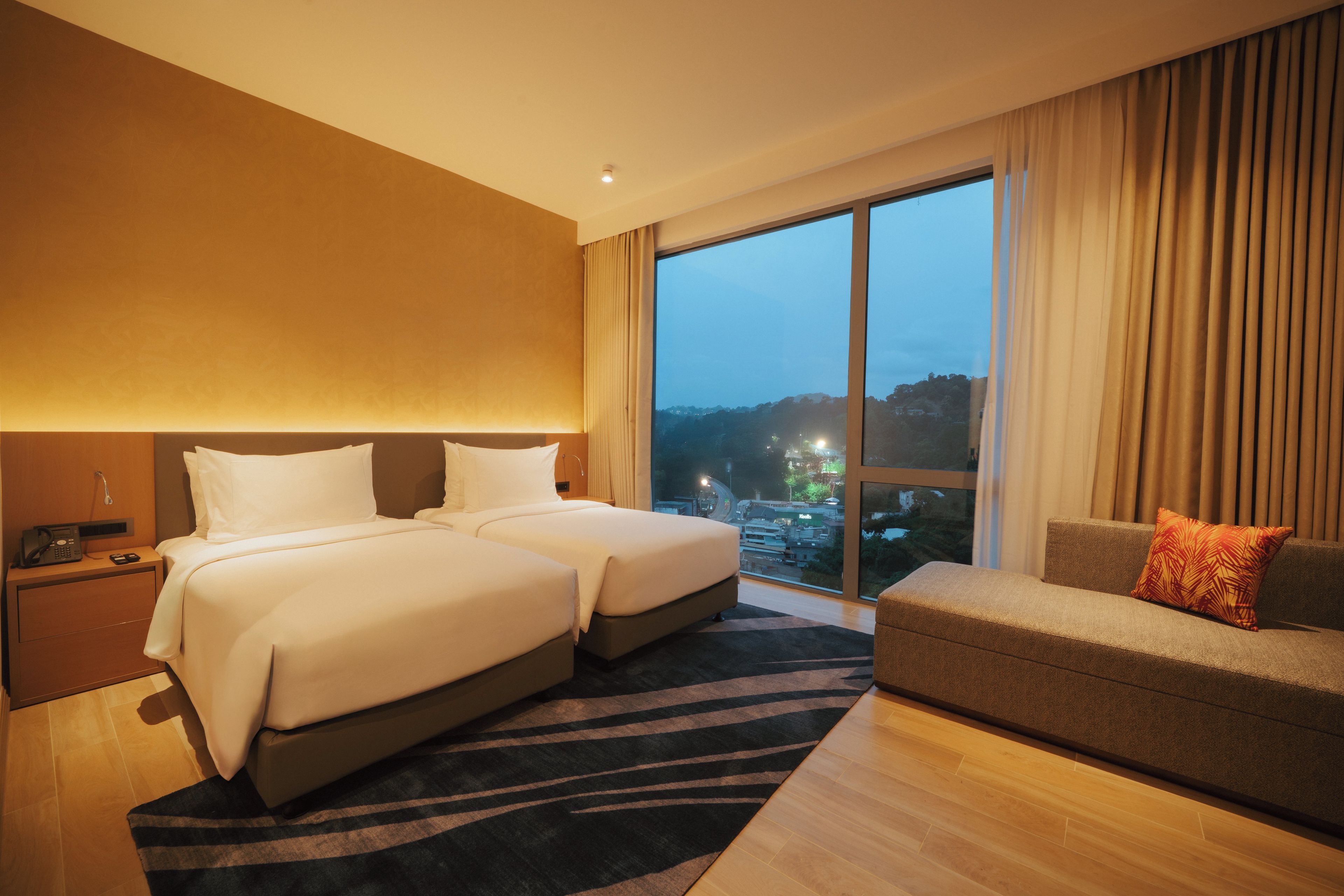 Habitación de hotel con dos camas, un sofá, un ventanal grande con vistas a la ciudad y un teléfono en la mesita de noche.