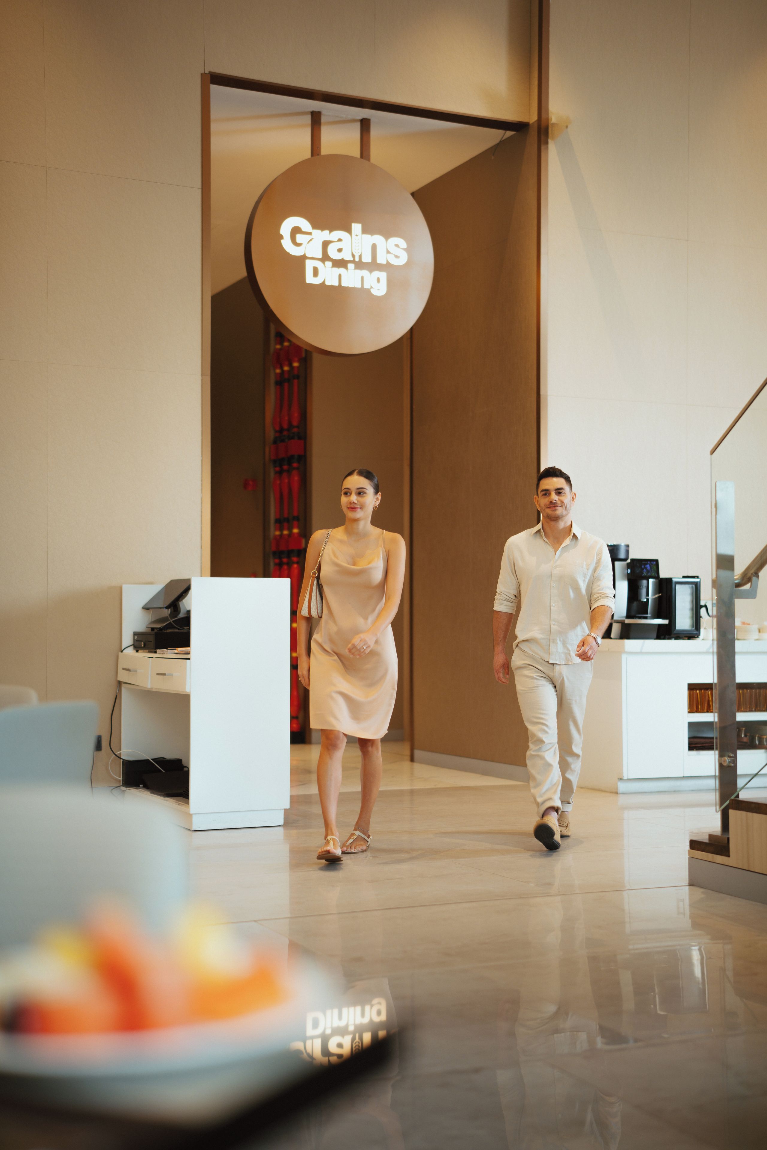 A modern interior with a sign reading 'Grains Dining' and a man and woman walking.