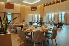 Un vaste espace dédié à la salle à manger, avec plusieurs tables rondes, des chaises confortables et de grandes fenêtres laissant entrer la lumière naturelle.