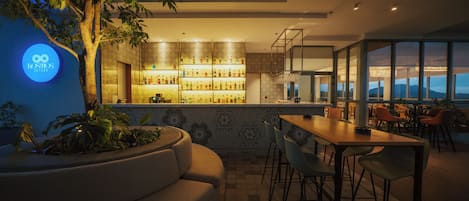 A modern bar area with a variety of liquor bottles, a seating arrangement with chairs and a table, and a large window offering a view.
