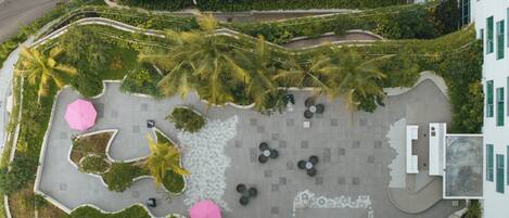 Vista aérea de un área ajardinada con palmeras, mobiliario y un camino pavimentado.