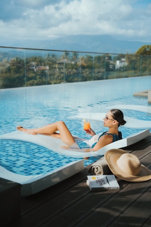 A person relaxing in a pool with a drink, a hat, and a book on a wooden deck.. Kandy Myst by Cinnamon