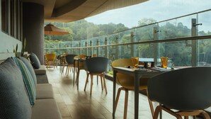 A modern dining area with a view of the outdoors, featuring a sofa, dining tables, chairs, and an umbrella. - Kandy Myst by Cinnamon (Kandy)