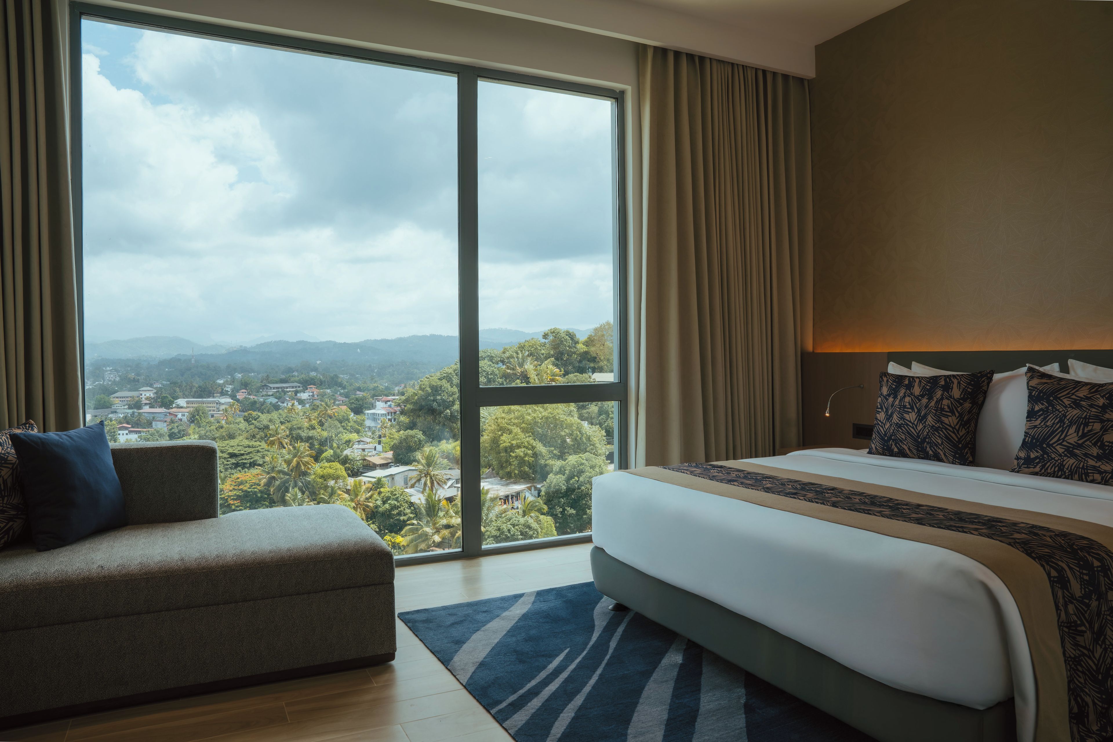 Habitación de hotel con un ventanal grande, una cama, un sofá y vistas a un paisaje urbano.