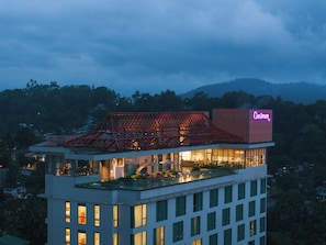 Un hôtel doté d’une terrasse sur le toit, d’une structure rouge imposante et d’une enseigne lumineuse au néon.
