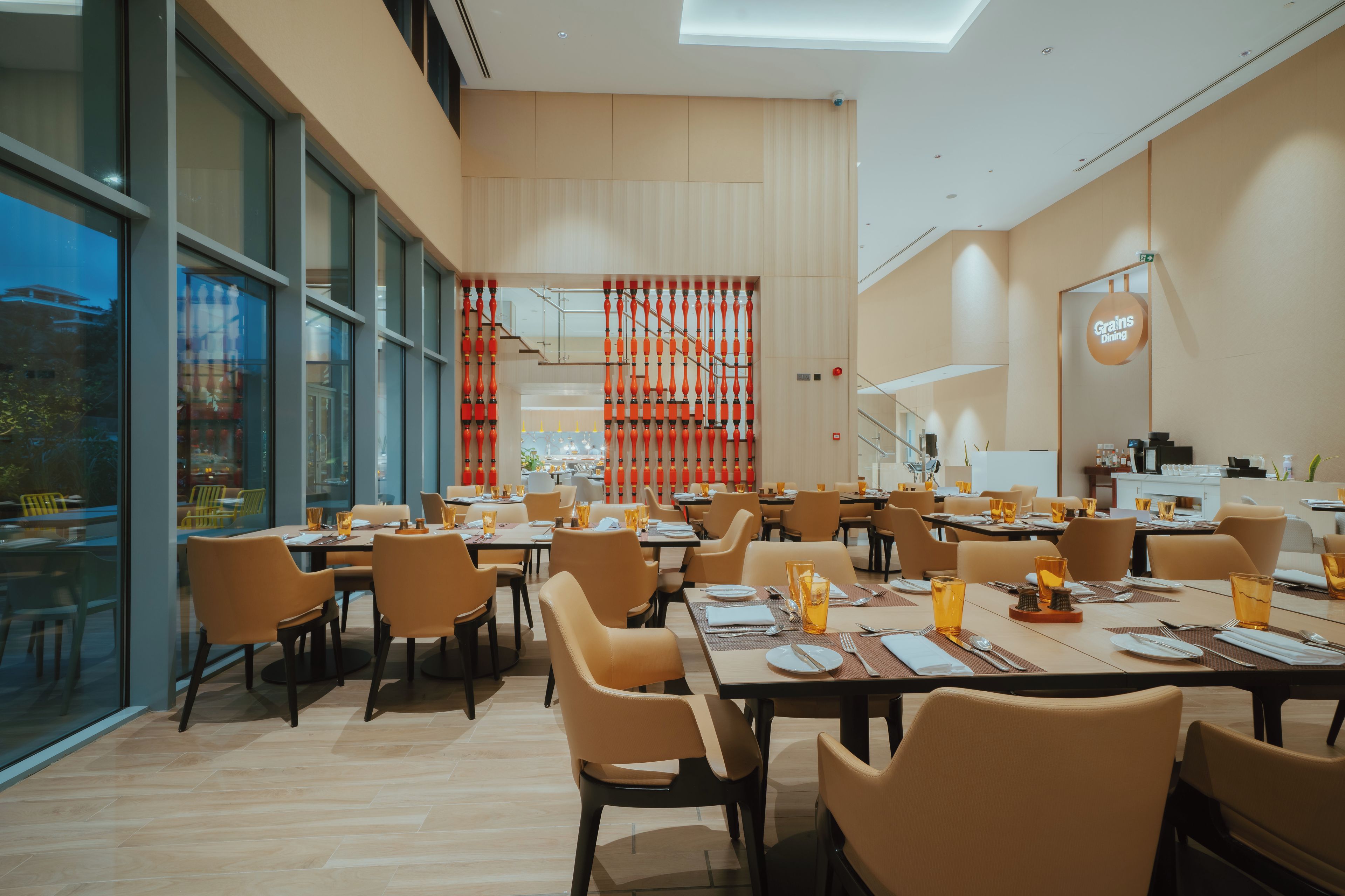 A modern dining area with multiple tables and chairs, large windows, and a view of the outside.
