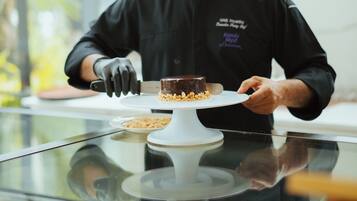 A chef in a black uniform with a tall white hat, cutting a chocolate dessert on a white plate.