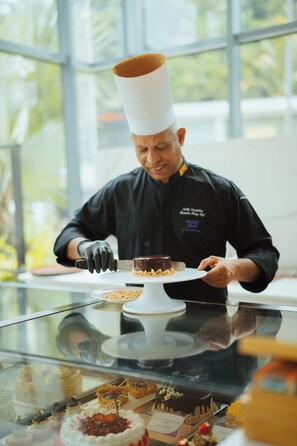A chef in a black uniform with a tall white hat, cutting a chocolate dessert on a white plate. - Kandy Myst by Cinnamon (Kandy)
