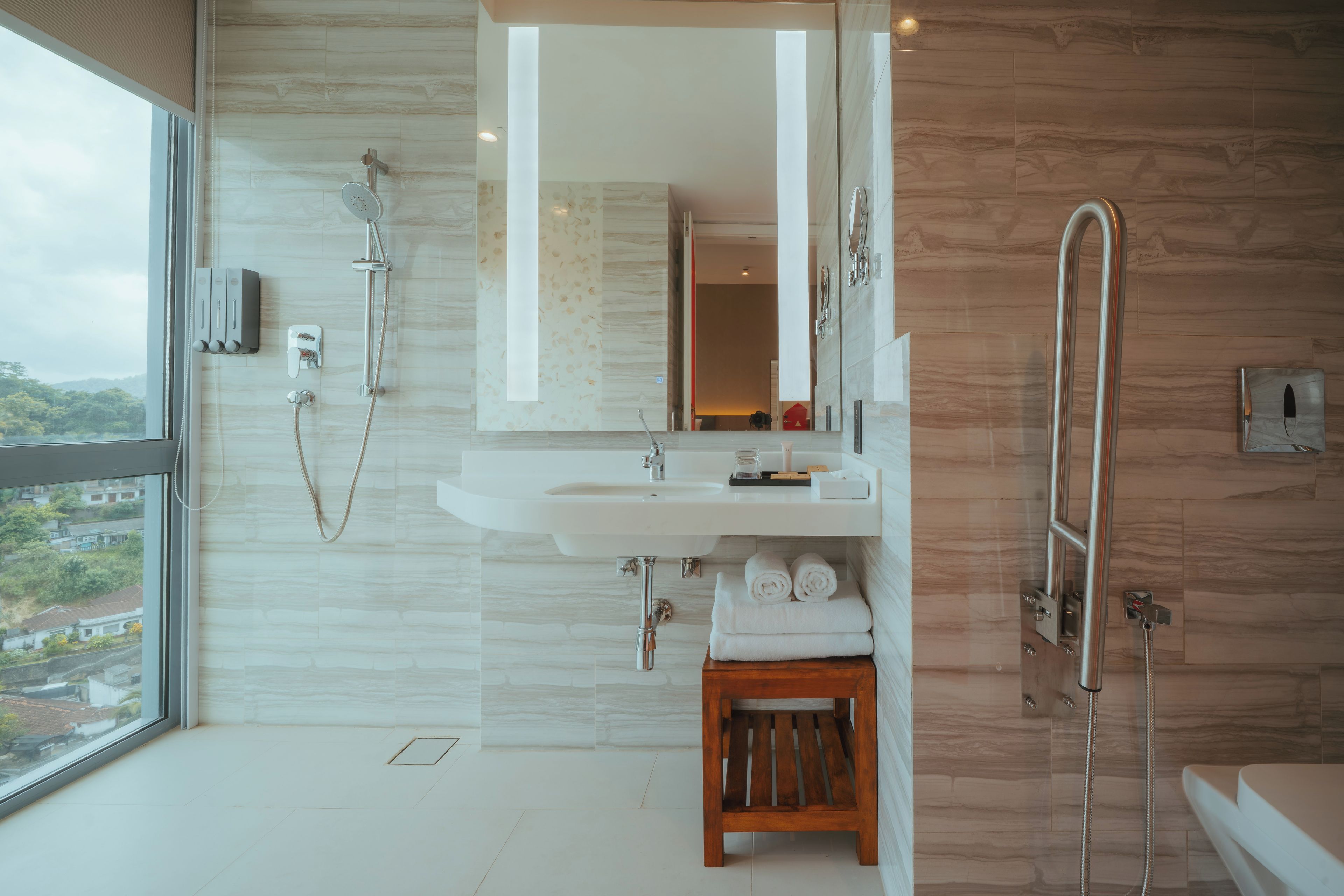 A modern bathroom with a large window, a shower, a sink, and a wooden stool.