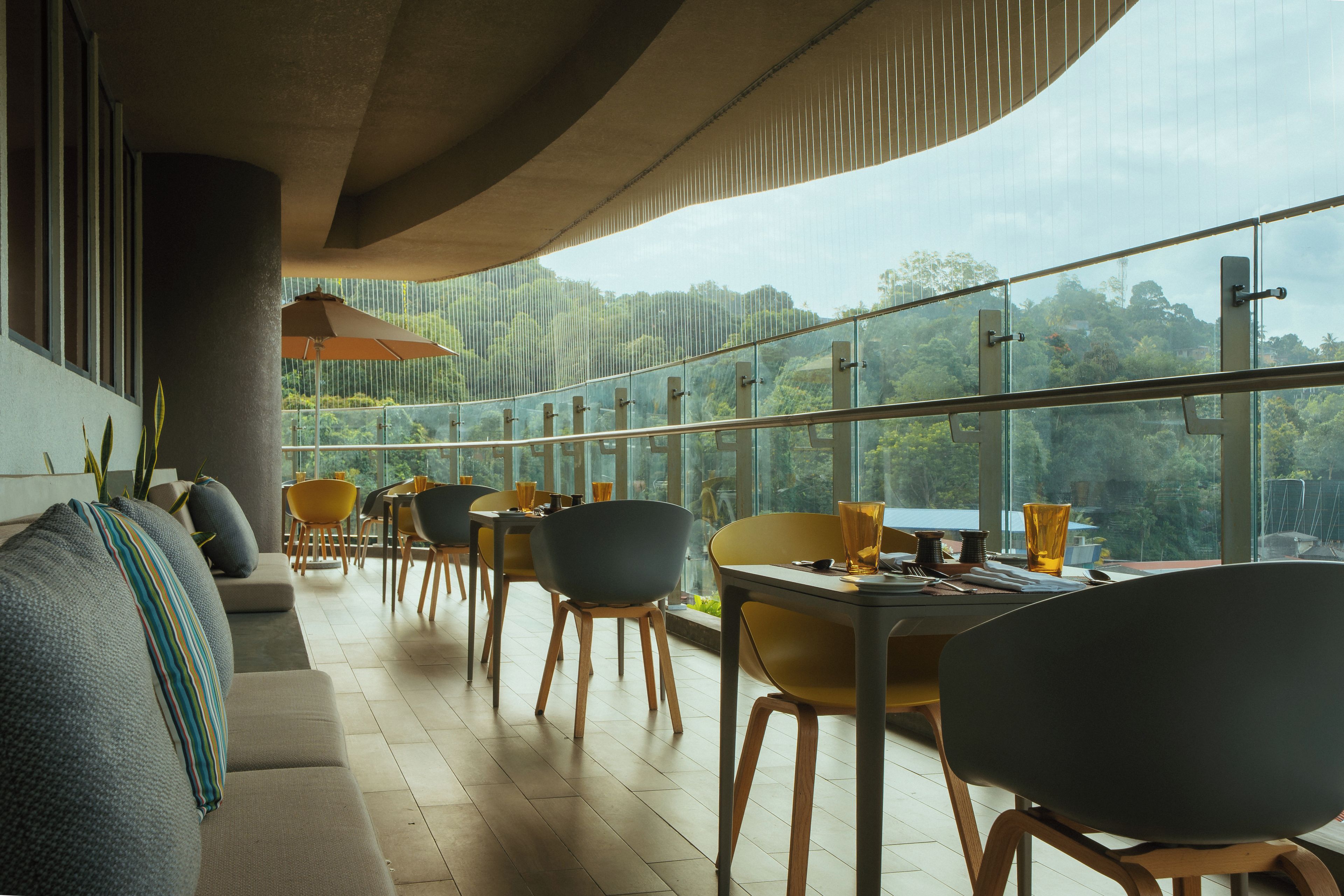 Uma área de refeições moderna com vista para o exterior, apresentando diferentes opções de assento e um guarda-corpo de vidro.