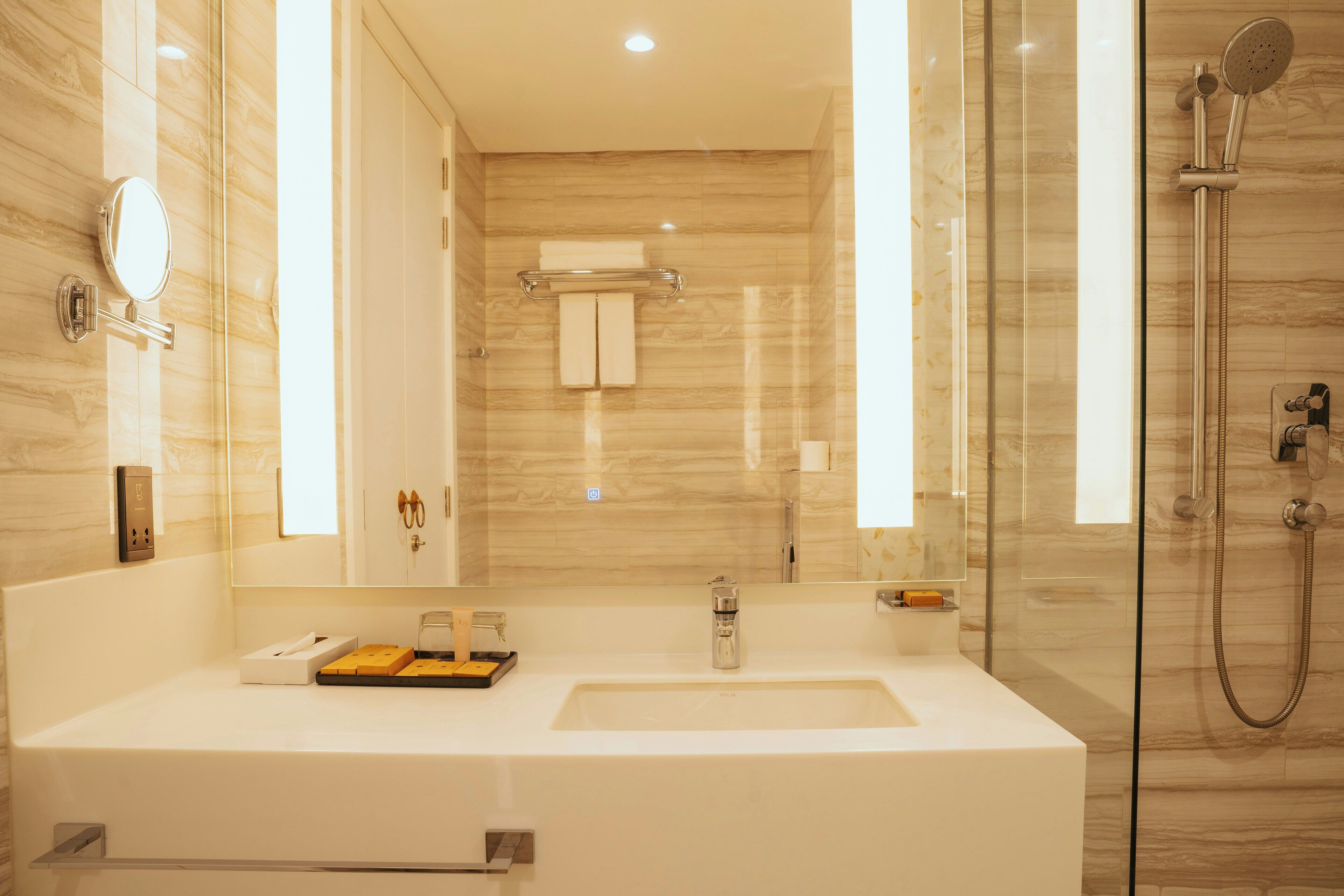 Une salle de bain moderne avec un grand miroir, un lavabo, une douche à parois de verre et un mur en marbre.