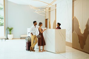 Un mostrador de recepción con una pared de mármol y diseño de paneles de madera. Se observa una planta en maceta y un banco al fondo.
