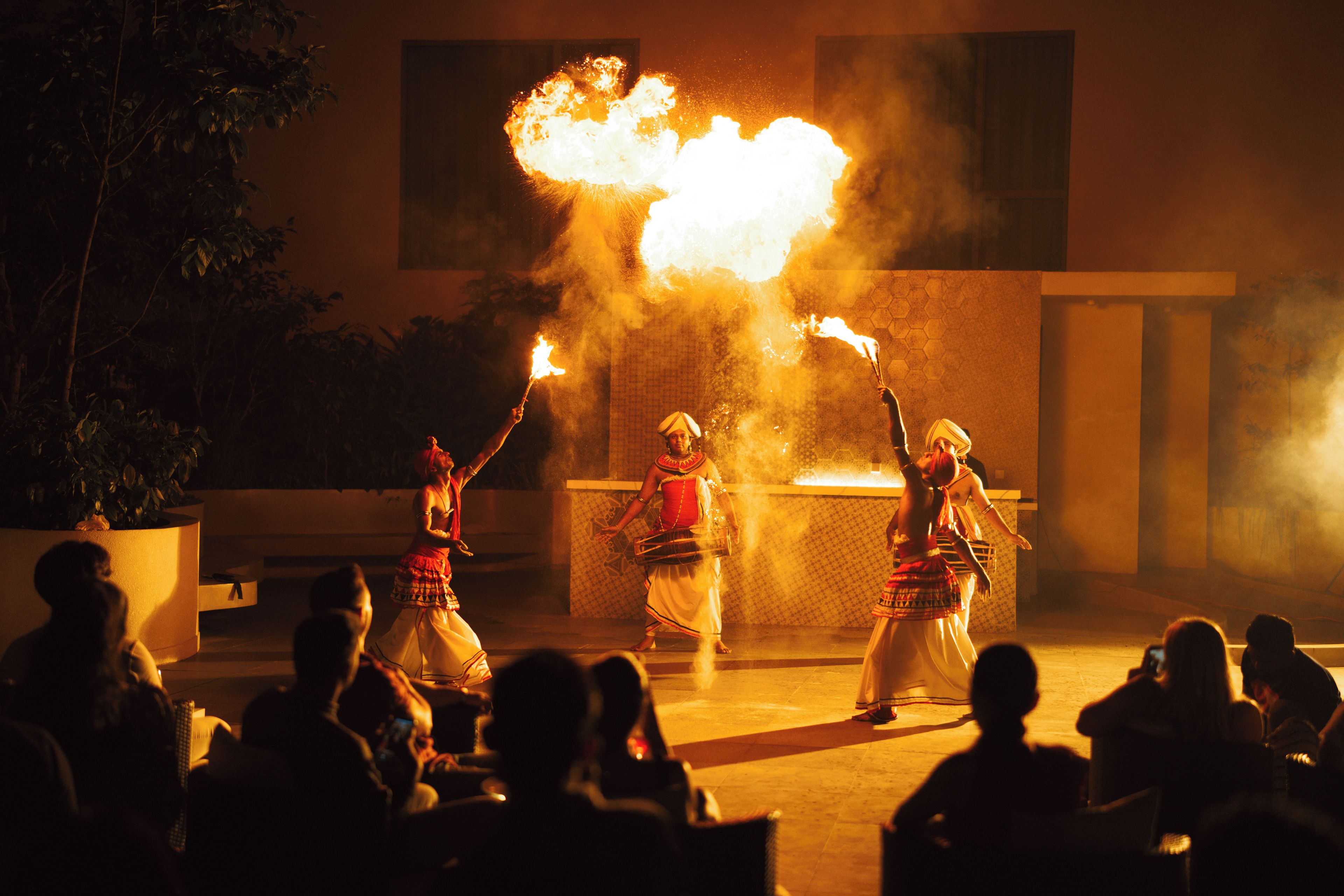 A performance with fire elements, audience in the foreground, and a building in the background.