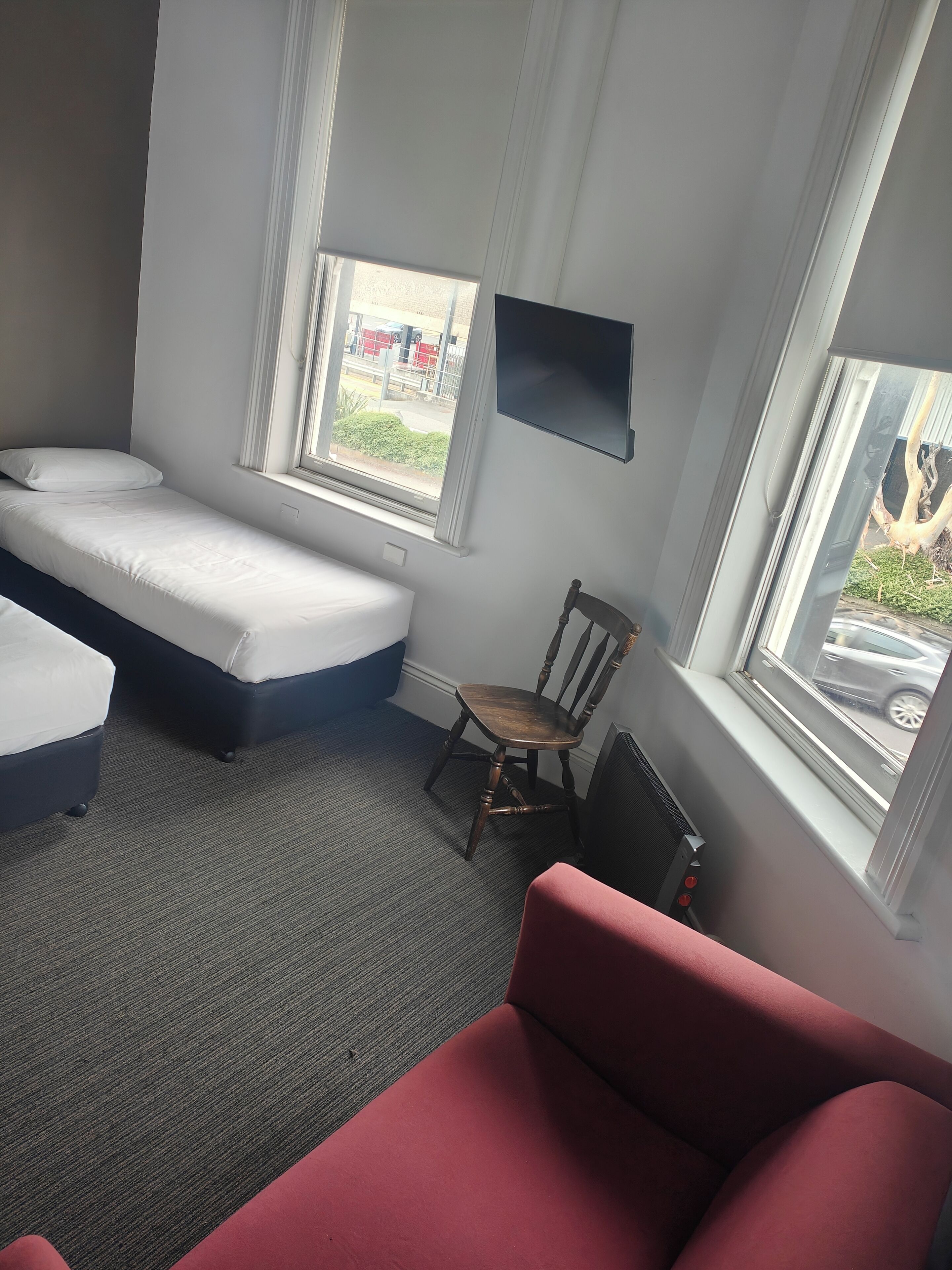 A room with a bed, a chair, and a red sofa. There are windows with views of the outside.