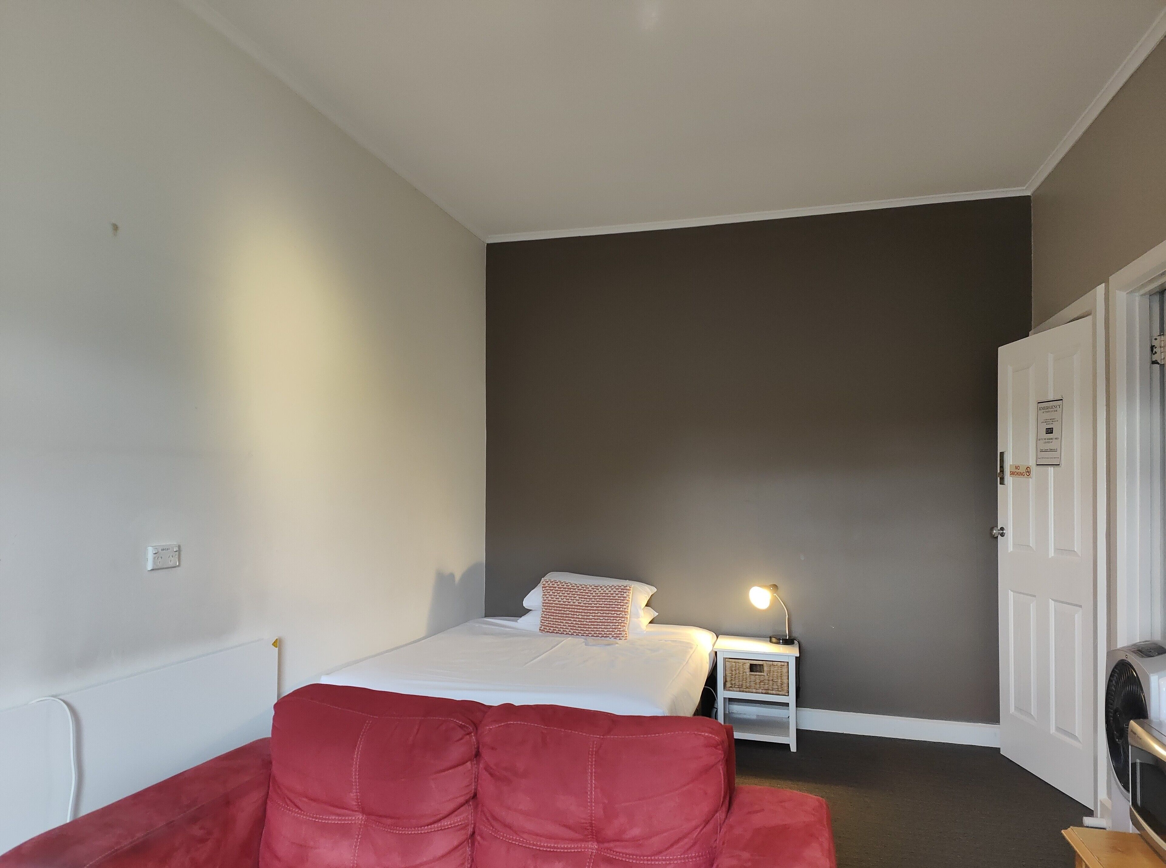 A bedroom with a bed, a nightstand, a lamp, a red chair, and a door.