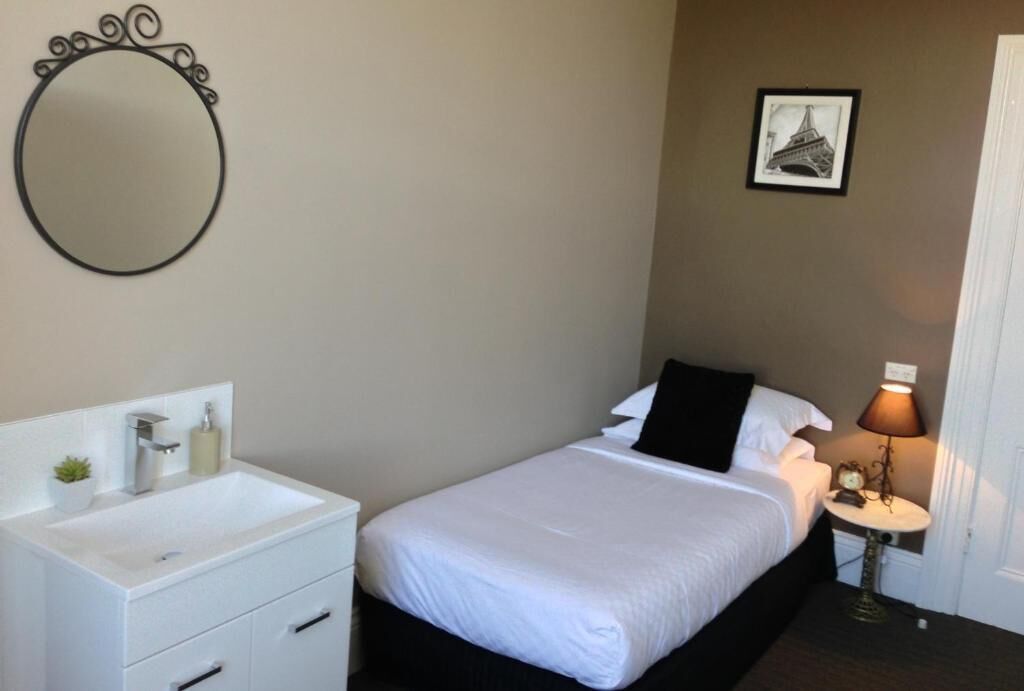 Un dormitorio con cama, mesita de noche, lámpara y espejo en la pared.