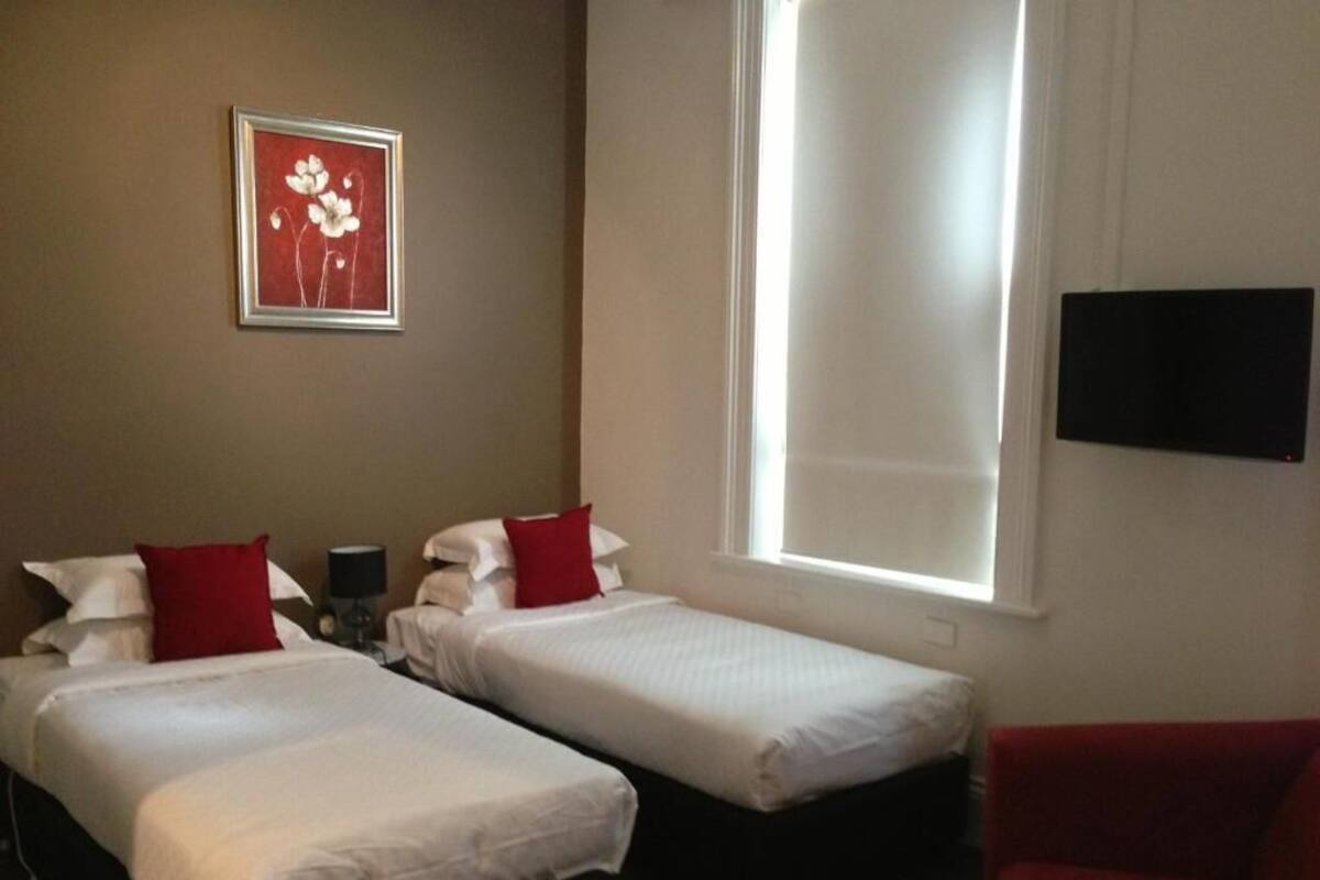 A hotel room with two beds, a red couch, a TV, and a window.