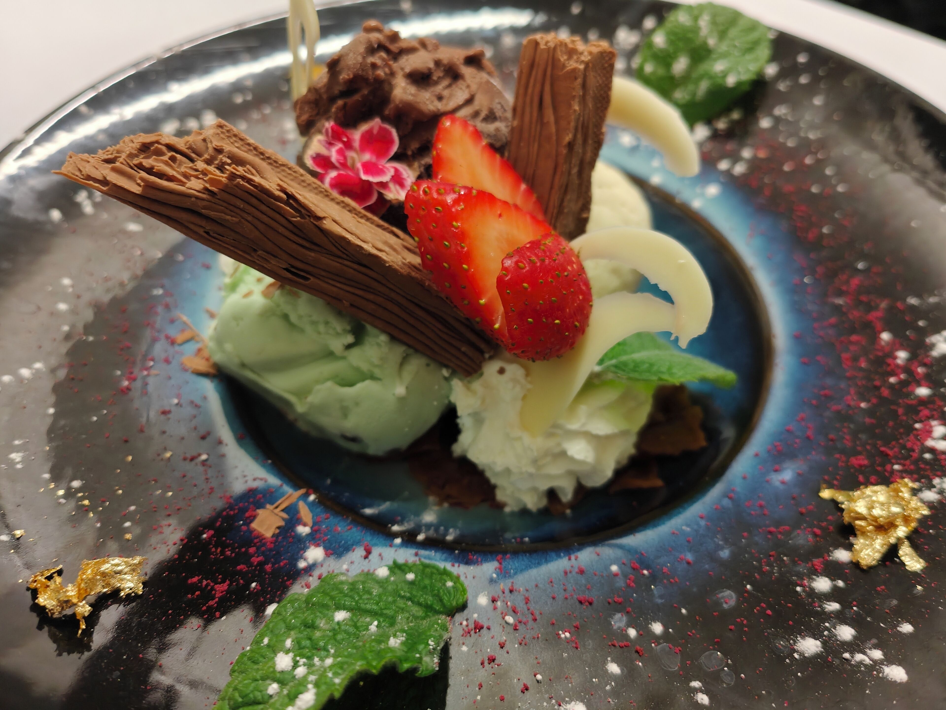 Un plato de postre con helado, fresas, chocolate y hojas de menta.