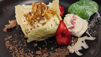 A dessert with whipped cream, crumbled cookies, and a strawberry on a black plate.