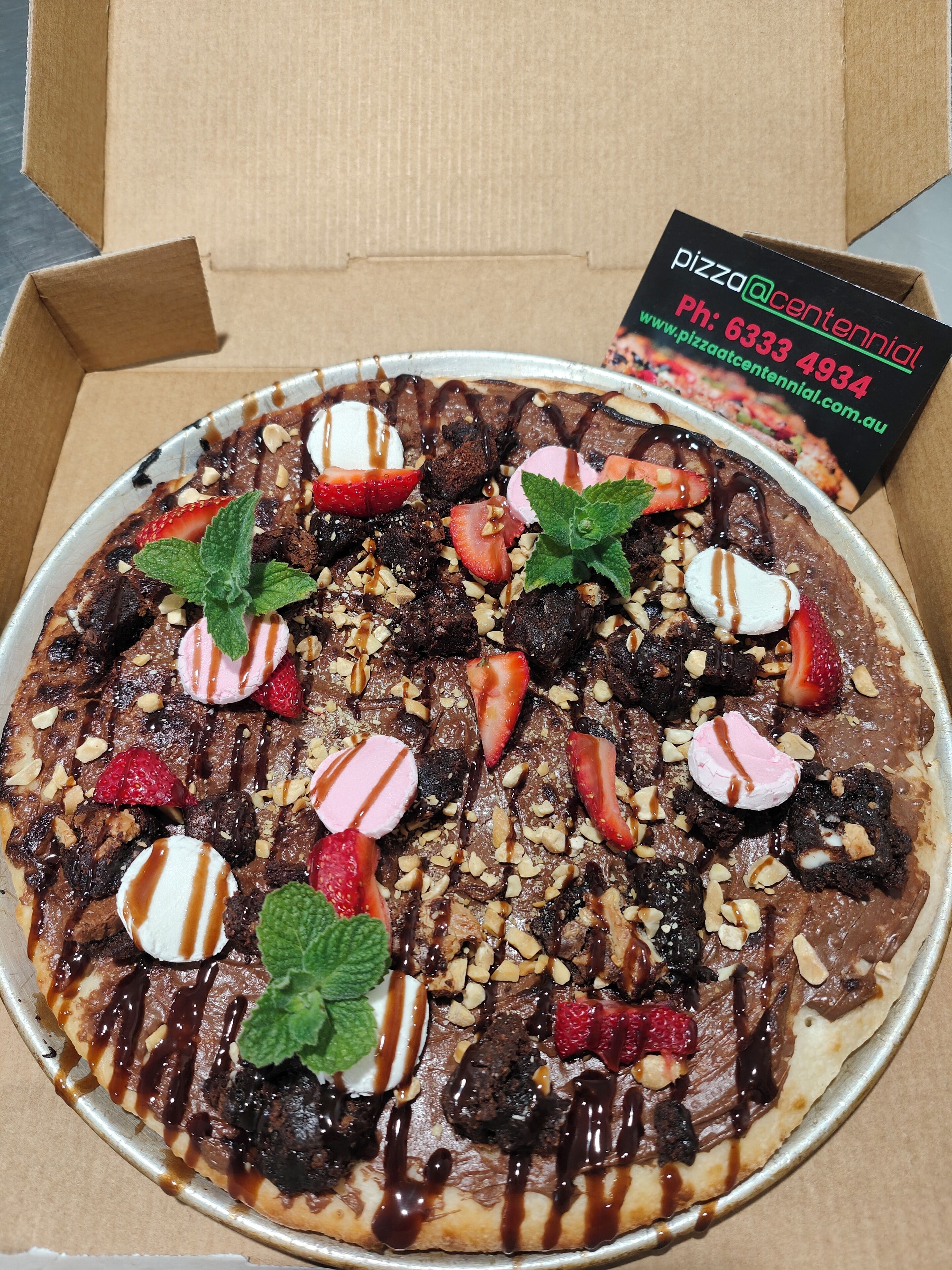 Una pizza con varios ingredientes y una tarjeta de presentación en una caja de cartón.