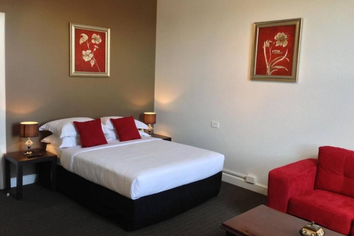 A hotel room with a large bed, two nightstands, a red sofa, and two framed floral artworks on the walls.