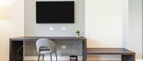A modern office space with a dark desk, a grey chair, a mounted TV, and a small plant on the desk.