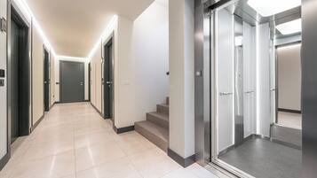 A modern hotel corridor with a clean, tiled floor and a staircase leading to an elevator.