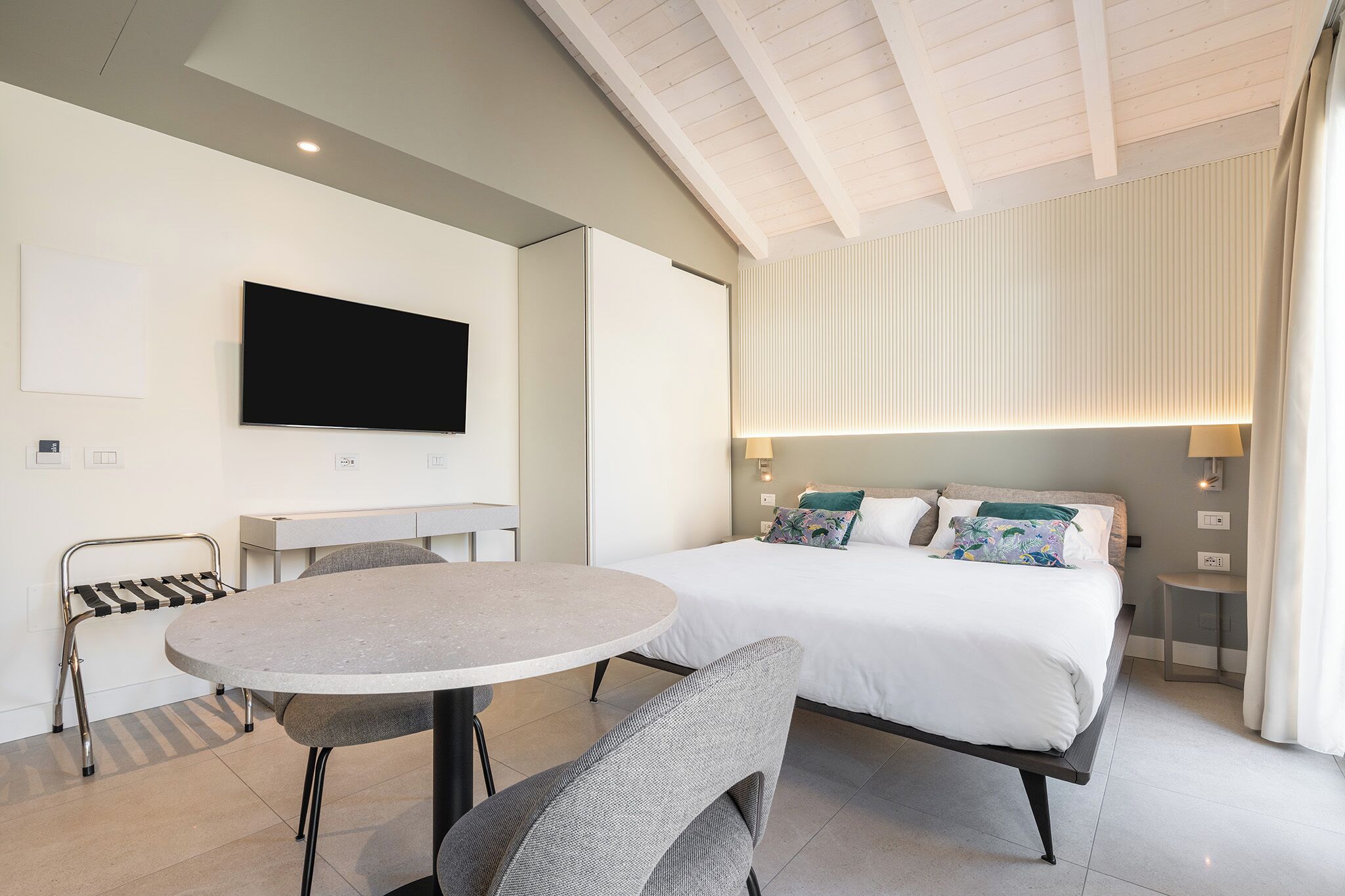 Une chambre d’hôtel moderne équipée d’un lit, d’une télévision, d’une table ronde et d’une chaise.