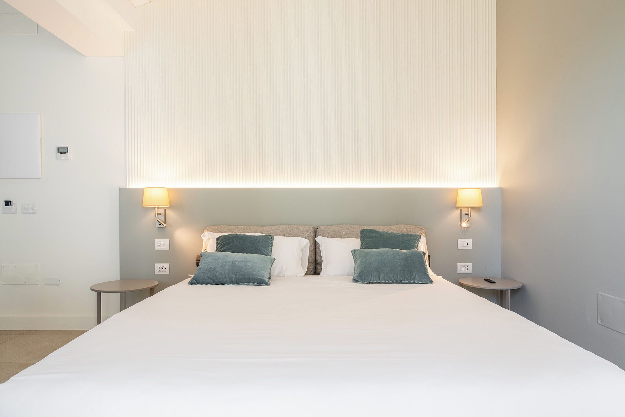 Een hotelkamer met een groot bed, twee nachtkastjes en wandlampen.