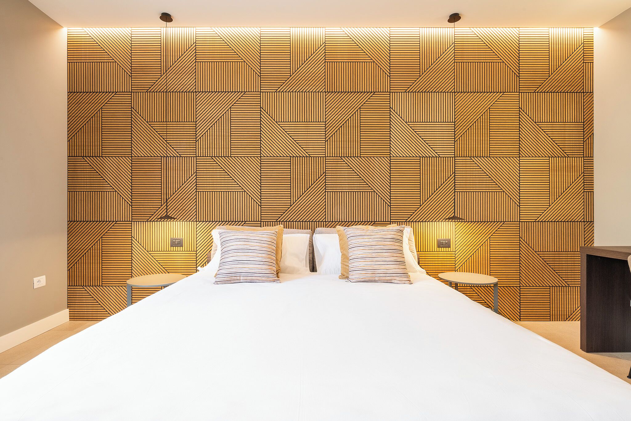 Une chambre d’hôtel moderne avec un grand lit, deux tables de chevet et une tête de lit ornée d’un motif géométrique.